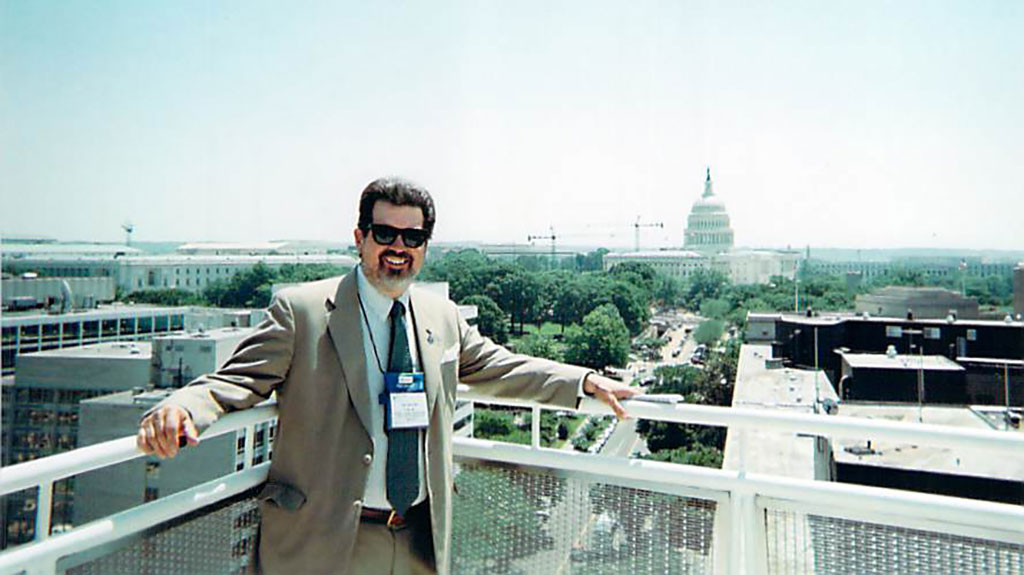 SIg buster standing on a balcony with the capital of DC in the background.